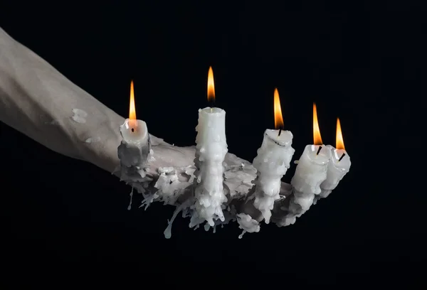 Halloween theme: on the hand wearing a candle and dripping melted wax on black isolated background