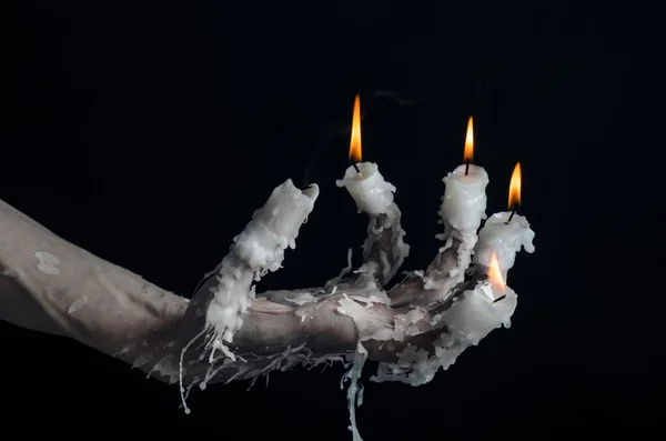 Halloween theme: on the hand wearing a candle and dripping melted wax on black isolated background