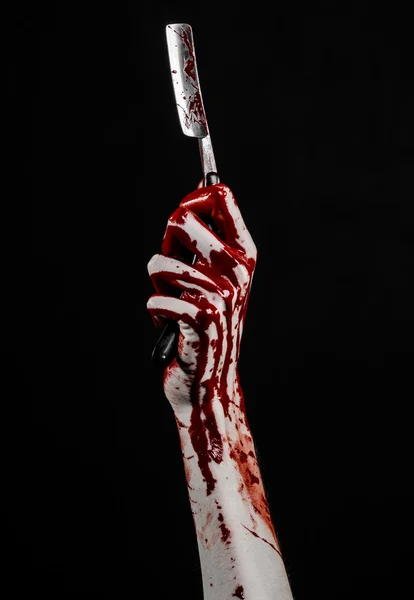 Bloody Halloween theme: bloody hand holds a razor sharp old with a dangerous edge isolated on black background