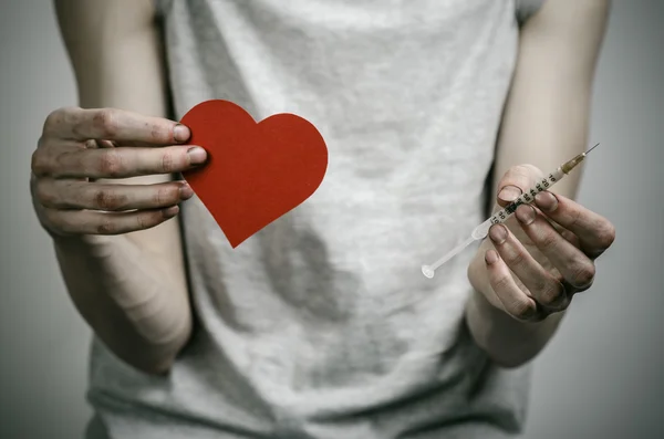 The fight against drugs and drug addiction topic: skinny dirty addict holding a syringe with a drug and red heart on a dark background