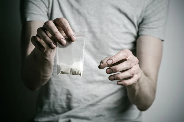 The fight against drugs and drug addiction topic: addict holding package of cocaine in a gray T-shirt on a dark background in the studio