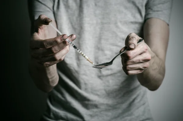 The fight against drugs and drug addiction topic: addict holding spoon lighter and heats the liquid drug in a T-shirt on a dark background