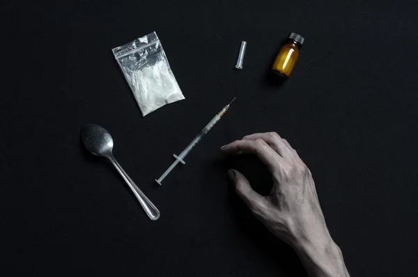 The fight against drugs and drug addiction topic: hand addict lies on a dark table and around it are drugs, a top studio