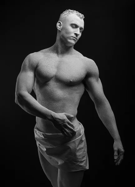 Statue and makeup body topic: inflated man with big muscles painted in white paint is cracked on a dark background