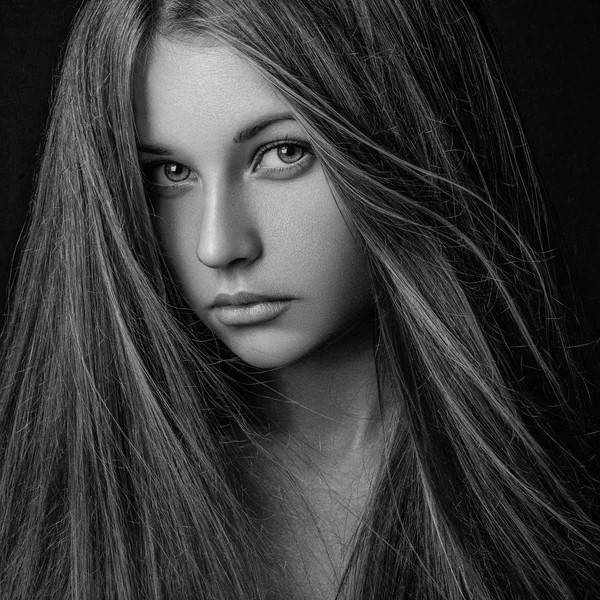 Dramatic portrait of a girl theme: portrait of a beautiful lonely girl with flying hair in the wind isolated on dark background in studio