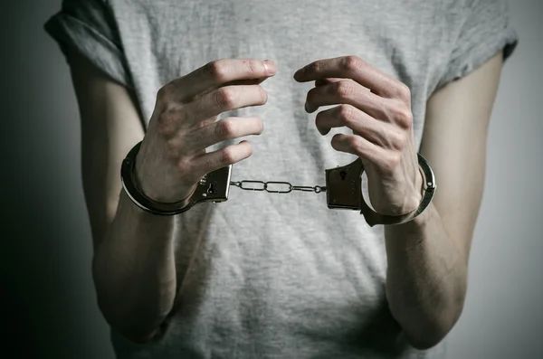 Prison and convicted topic: man with handcuffs on his hands in a gray T-shirt on a gray background in the studio, put handcuffs on rapist