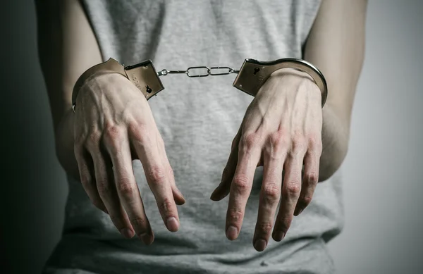 Prison and convicted topic: man with handcuffs on his hands in a gray T-shirt on a gray background in the studio, put handcuffs on rapist