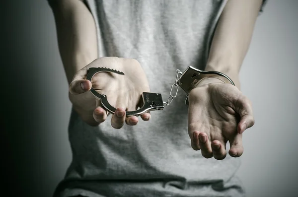 Prison and convicted topic: man with handcuffs on his hands in a gray T-shirt on a gray background in the studio, put handcuffs on rapist