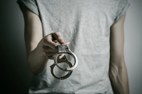 Prison and convicted topic: man with handcuffs on his hands in a gray T-shirt on a gray background in the studio, put handcuffs on rapist