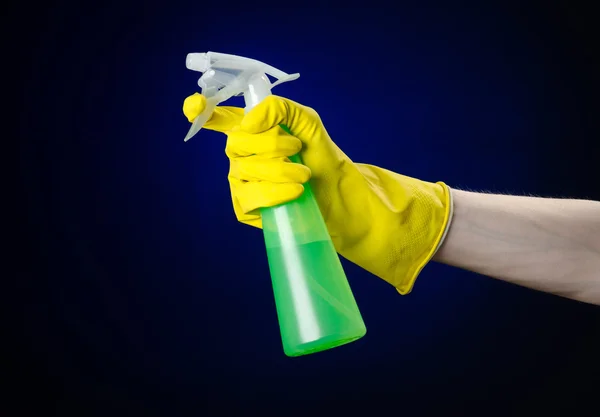 Cleaning the house and cleaner theme: man\'s hand in a yellow glove holding a green spray bottle for cleaning on a dark blue background