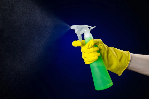 Cleaning the house and cleaner theme: man\'s hand in a yellow glove holding a green spray bottle for cleaning on a dark blue background