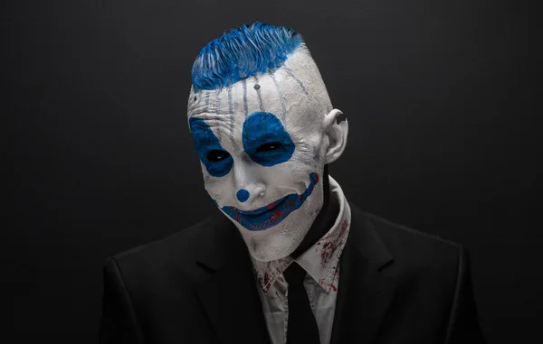 Terrible clown and Halloween theme: Crazy blue clown in black suit isolated on a dark background in the studio