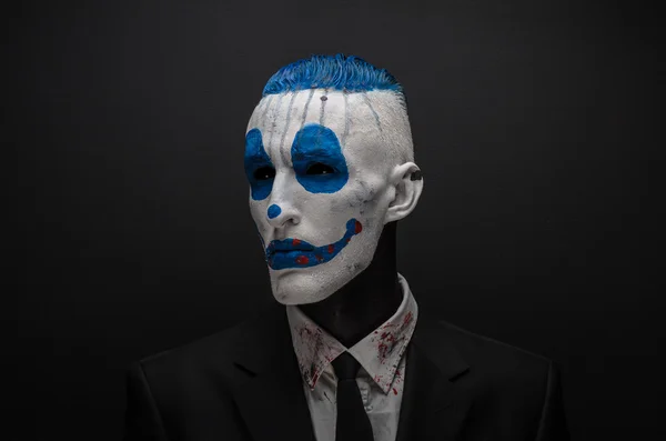 Terrible clown and Halloween theme: Crazy blue clown in black suit isolated on a dark background in the studio