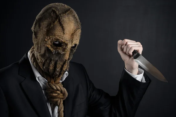 Fear and Halloween theme: a brutal killer in a mask holding a knife on a dark background in the studio