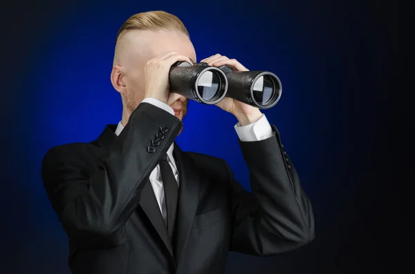 Business and search topic: Man in black suit holding a black binoculars in hand on a dark blue background in studio isolated