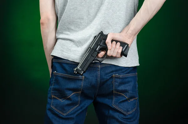 Firearms and murderer topic: man in a gray t-shirt holding a gun on a dark green background isolated in studio