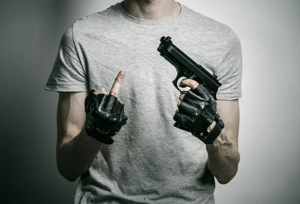Horror and firearms topic: the killer with a gun in his hand in black gloves on a gray background in the studio