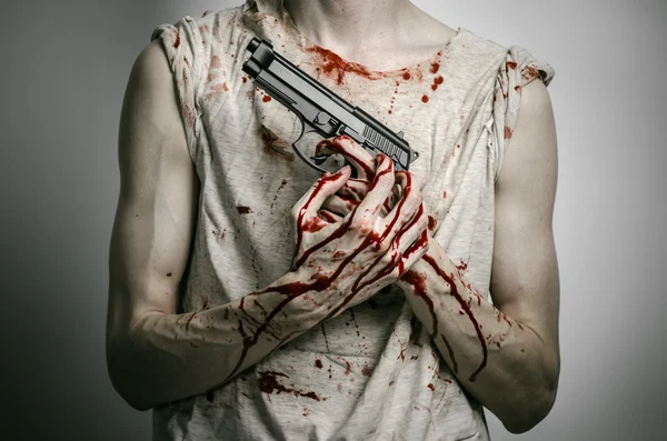 Horror and firearms topic: the bloody killer with a gun on a gray background in the studio