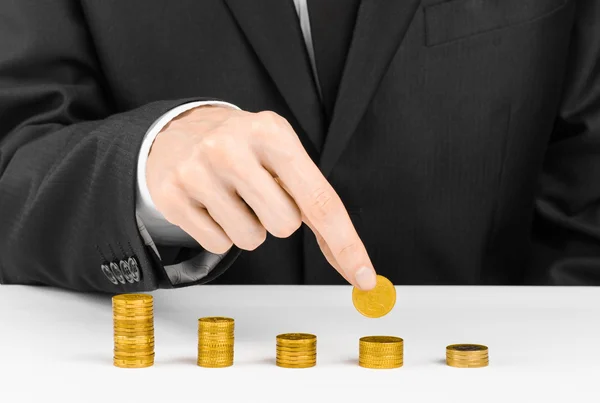 Money and business theme: a man in a black suit indicates the chart bars of gold coins on a white table in the studio on a white background isolated