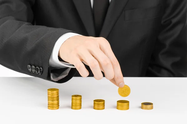 Money and business theme: a man in a black suit indicates the chart bars of gold coins on a white table in the studio on a white background isolated