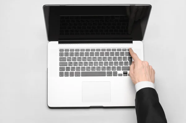 Business and technology topic: the hand of man in a black suit showing gesture against a gray and white background laptop in the studio isolated top view