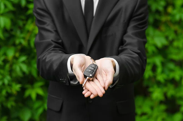 New car and business theme: a man in a black suit holds the keys of a new car on a background of green grass