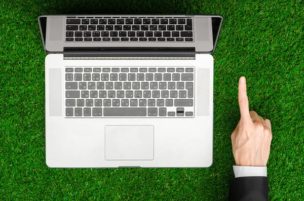 Work outdoors and businessman topic: human hands show the gestures in a black suit and an open notebook on a background of green grass top view