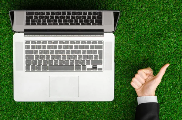 Work outdoors and businessman topic: human hands show the gestures in a black suit and an open notebook on a background of green grass top view