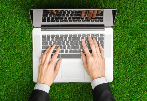 Work outdoors and businessman topic: human hands show the gestures in a black suit and an open notebook on a background of green grass top view