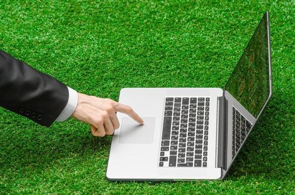 Work outdoors and businessman topic: human hands show the gestures in a black suit and an open notebook on a background of green grass