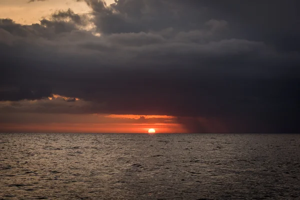 Sun setting between sea and black stormclouds