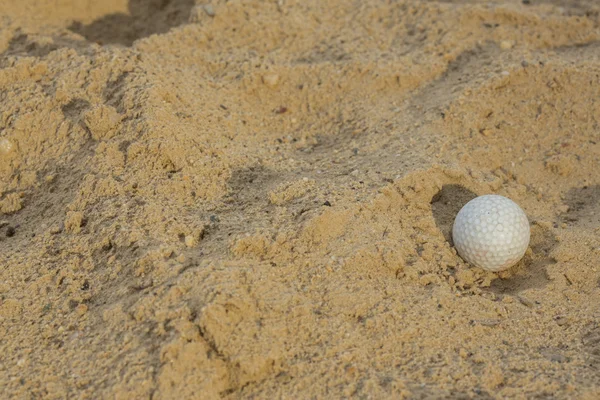 Sunlit golf ball with shadow in unraked sand trap. Macro with sh