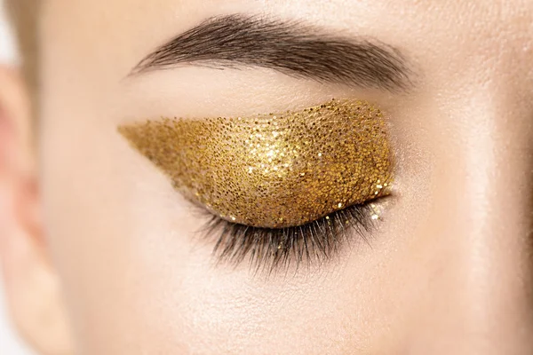 Macro female closed eye with gold glitter on the eyelid