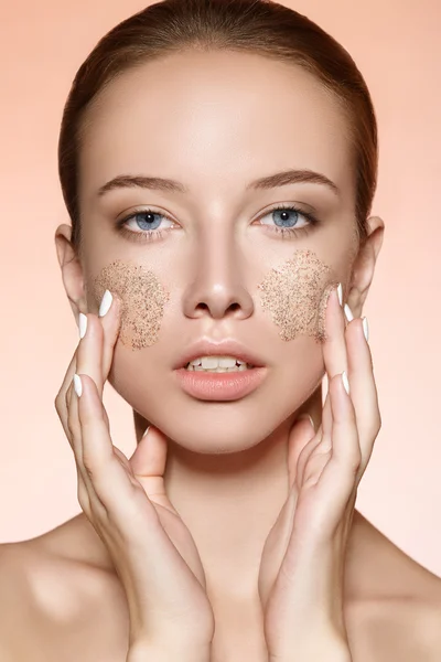 Attractive young girl rubs a skin scrub on the cheeks