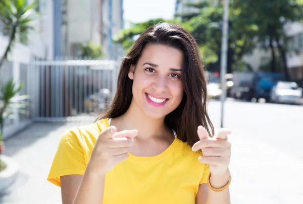 Caucasian woman in yellow shirt in the city pointing at camera