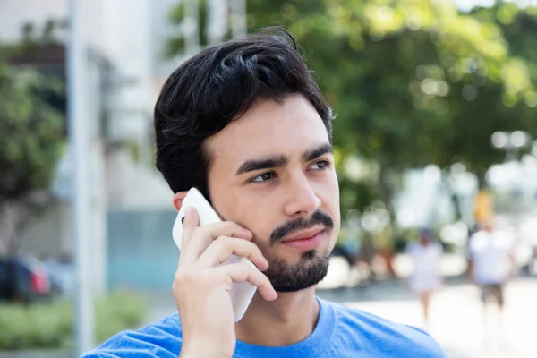 Thinking hispanic guy listening at phone in city