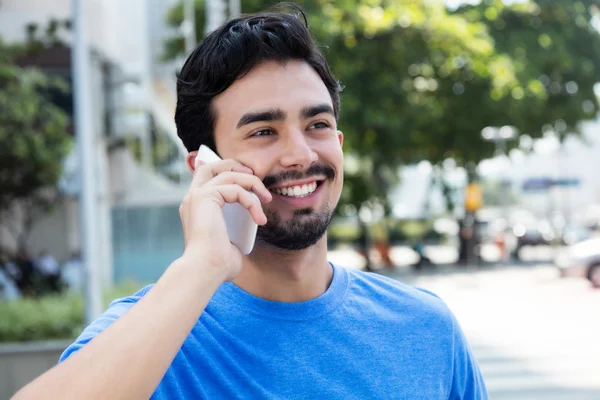 Happy hispanic guy at phone in city