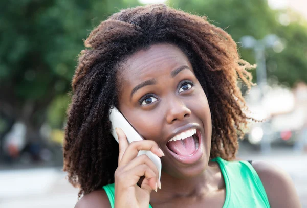 Happy african woman in a green shirt outdoor at phone
