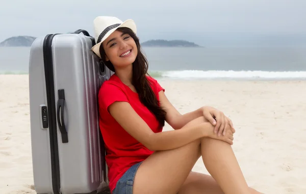 Laughing caucasian female tourist with suitcase at beach