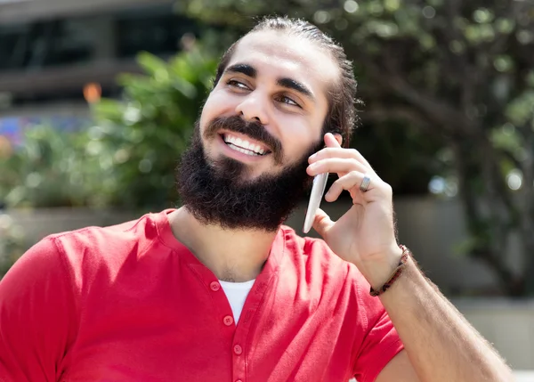 Arabian guy with beard and red shirt at phone in city