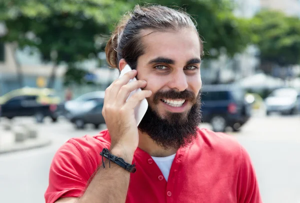 Smiling arabian guy with beard and red shirt at phone in city