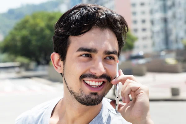 Happy hispanic guy in a grey shirt at phone in city