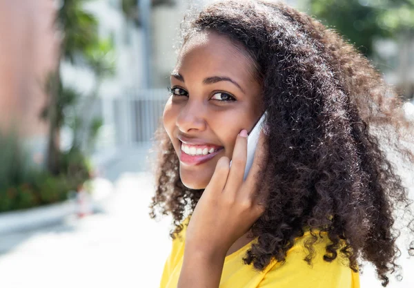 Smiling latin woman with curly hair at phone in summer