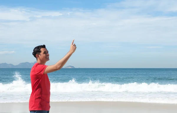 Laughing latin guy at beach pointing at sky