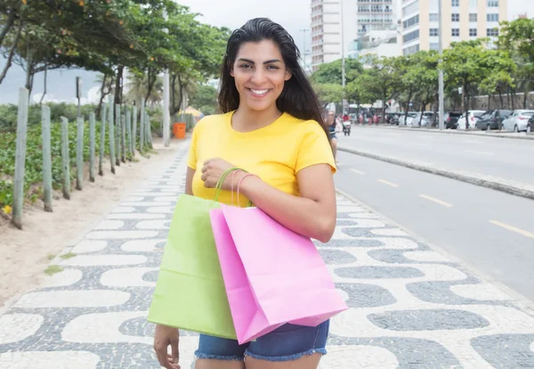 Latin woman with yellow shirt and shopping bags in city