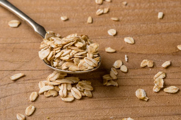 Oat flakes on wooden table with steel spoon
