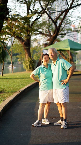 Asian senior couple relaxing in the park laughing in sunshine