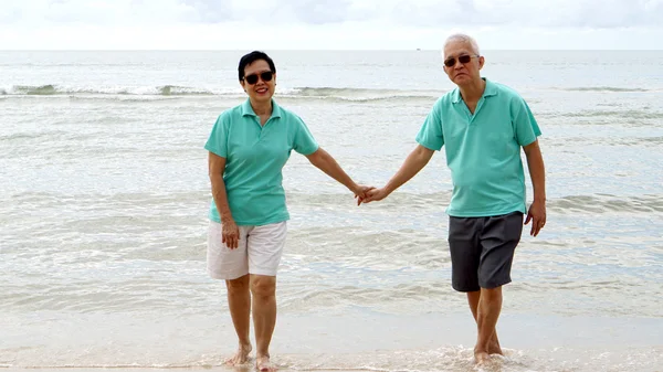 Asian senior couple walking together on the beach by the sea