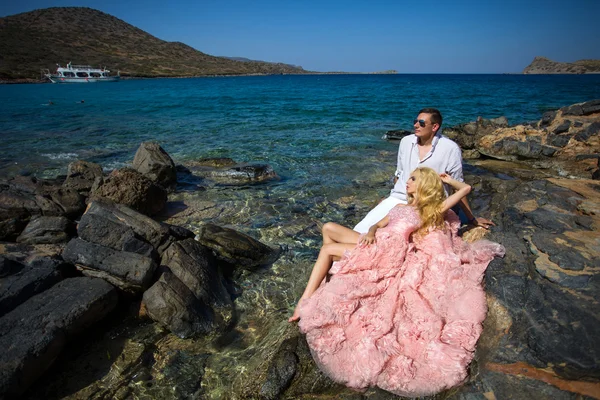 Beautiful blond woman sexy pink ballroom dress standing on the rocks in Santorini