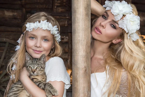 A beautiful blond woman with a baby girl snuggling on the wild west in white costumes with a cat on hands